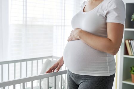 Pregnant woman standing next to a baby cribの写真素材