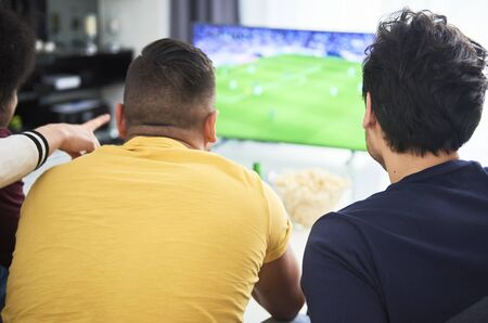Rear view of men watching a match on TV at homeの写真素材