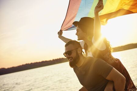 Happy man carrying woman with rainbow flag by seaの写真素材