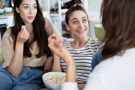 Surprised friends talking and eating popcornの写真素材