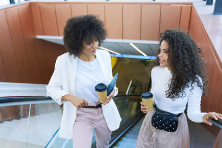 Two businesswomen riding escalator outdoorsの写真素材