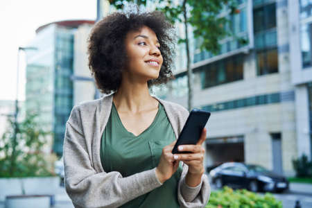 African woman looking around while holding the phone