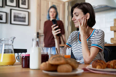Smiling lesbian sending text messages during breakfastの写真素材