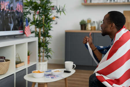 Cheerful man watching TV and holding American flag