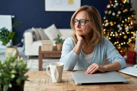 Worried mature woman sitting in front of laptop at home.の写真素材