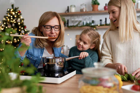 Grandma together with her daughter and granddaughter tasting Christmas dishesの写真素材