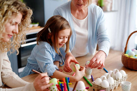 Mother grandmother and granddaughter decorate easter eggs togetherの写真素材