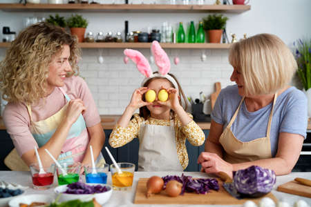 Girl with mother and grandmother have fun during coloring eggs