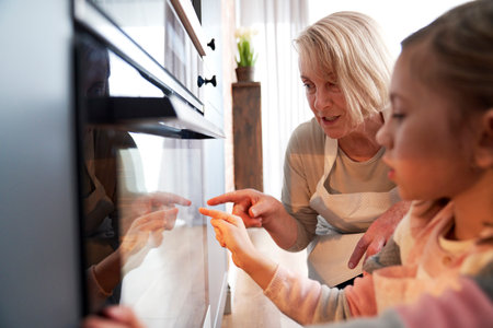 Grandma and granddaughter watching Easter biscuits in kitchen ovenの写真素材