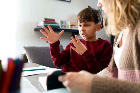 Boy gesturing during doing homework with his motherの写真素材
