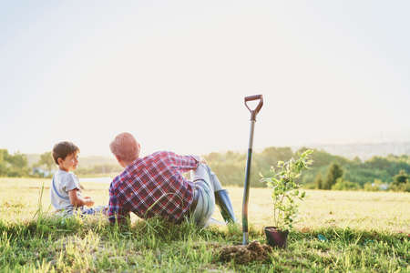 Grandfather and grandson sitting in the meadow at sunsetの写真素材