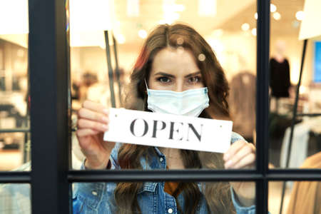 Woman in protective mask holding open sign in store windowの写真素材