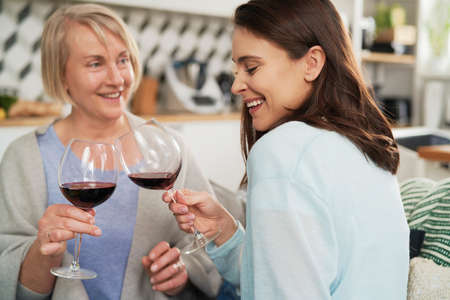 Happy adult daughter and senior mother toasting in wine