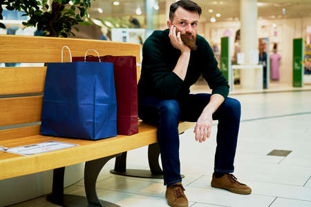 Bored man sitting on bench in shopping mallの写真素材