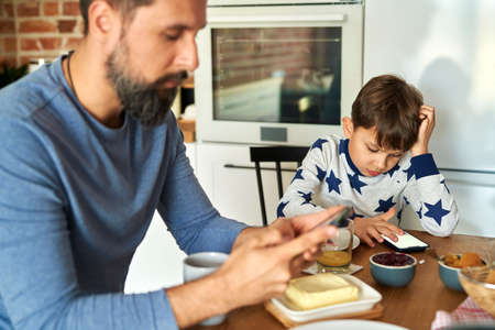 Father and son sitting with mobile phone while breakfast