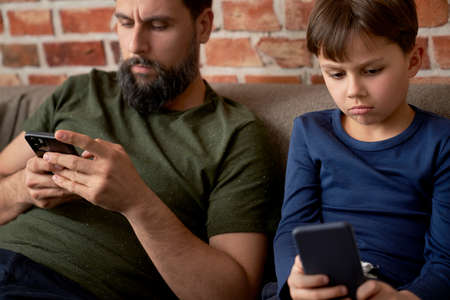 Close up of boredom father and son using mobile phoneの写真素材