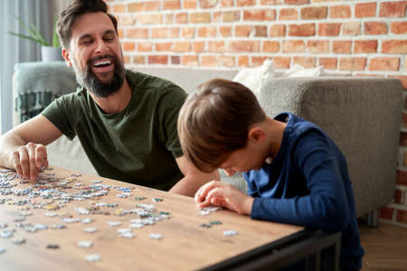 Happy son and father having fun during solving jigsaw puzzleの写真素材
