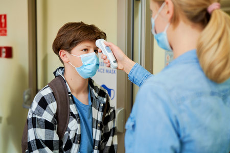 Teacher checking the temperature of the students before entering the school