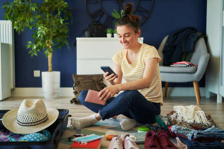 Happy woman using phone during preparing to travelの写真素材