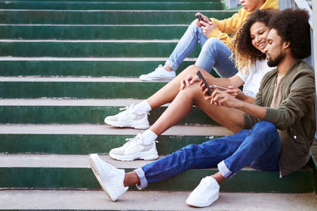 Side view of young people sitting on stairs with phonesの写真素材