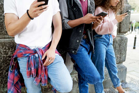 Close up of unrecognizable young people standing with mobile phonesの写真素材
