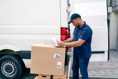 Courier standing with packages and looking at documentsの写真素材
