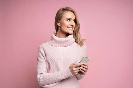 Studio shot of cheerful caucasian young woman holding phone and looking at copy spaceの写真素材