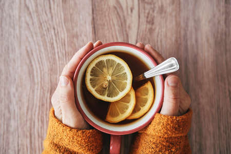Top view of human hands holding cup of hot tea