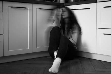 Black and white image of thoughtful young caucasian woman sitting on floor in the kitchenの写真素材