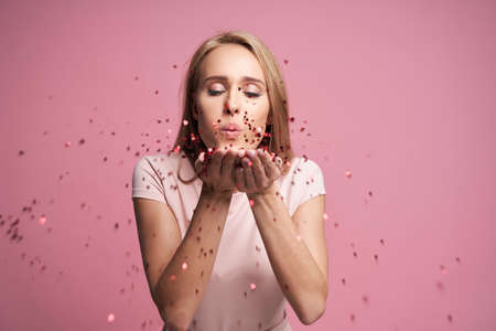Blonde woman blowing little heart shaped confettiの写真素材