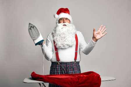 Shocked caucasian Santa Claus ironing trousers for Christmasの写真素材