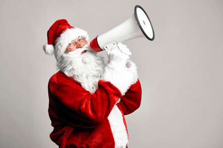 Caucasian Santa Claus talking by megaphone on gray background