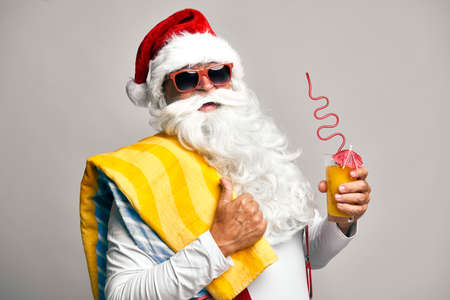 Caucasian Santa Claus with drink and sunglasses on gray backgroundの写真素材