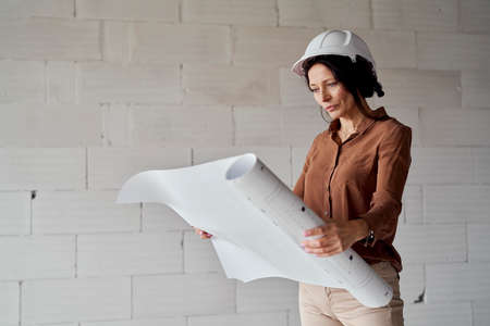 Female mature caucasian engineer standing on construction site and browsing building plansの写真素材