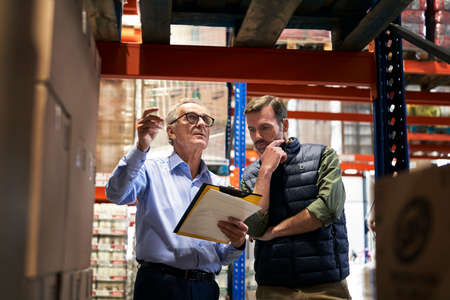 Two caucasian men in mature age discussing over documents together in warehouseの写真素材