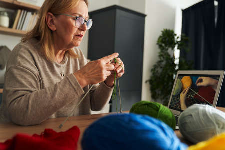 Senior caucasian woman at home learning how to knit from video tutorialの写真素材