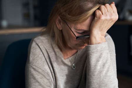 Thoughtful caucasian senior woman sitting in the kitchenの写真素材