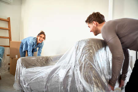 Caucasian young couple lifting sofa while moving house