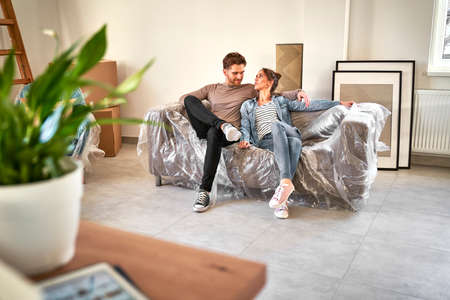 Happy caucasian couple sitting on sofa while moving houseの写真素材