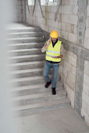 Caucasian engineer walking on stairs and browsing digital tablet on construction site