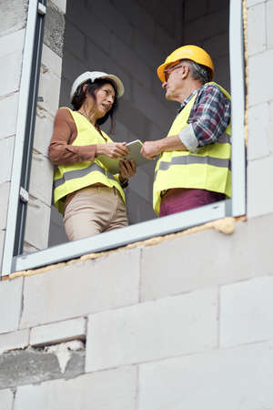 Two caucasian engineers standing near to window and discussing over digital tablet on the...