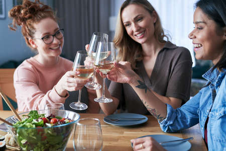 Three female caucasian friends making toast with a glass of wine at homeの写真素材