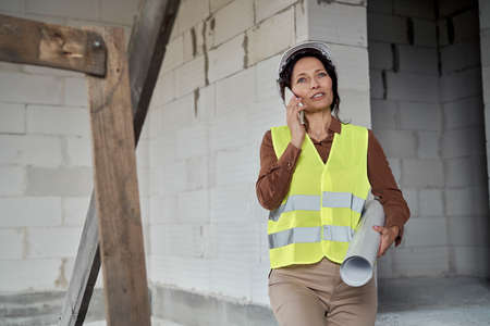 Female mature caucasian engineer moving on the stairs on construction site and talking one mobile phoneの写真素材