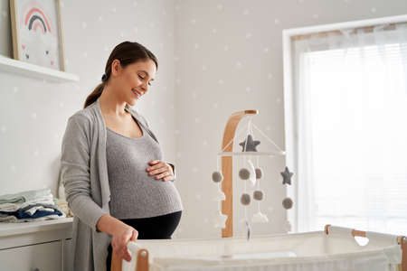Caucasian woman in advanced pregnancy standing in the baby's room next to the cribの写真素材