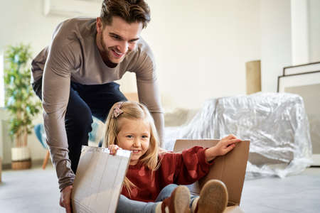 Caucasian father pushing little girl in paper box while moving houseの写真素材