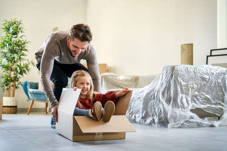 Caucasian father pushing little girl in paper box while moving houseの写真素材