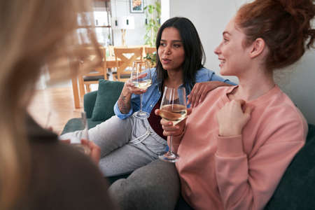Three female caucasian friends chatting and drinking wine at homeの写真素材