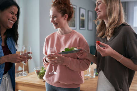 Three female caucasian friends gossiping and drinking wine at homeの写真素材