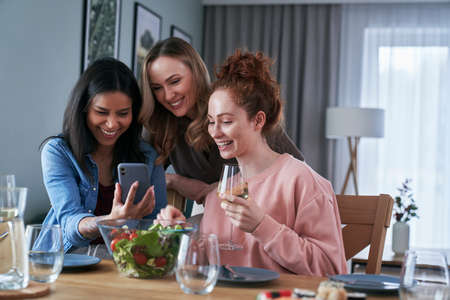 Three caucasian friends smiling while browsing smart phoneの写真素材