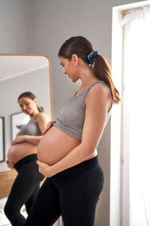 Caucasian woman in advanced pregnancy browsing herself in the mirrorの写真素材